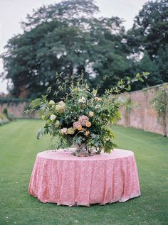 a pink table with flowers and greenery on it in the middle of a field