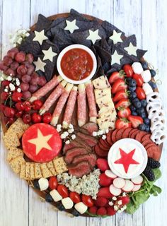 a platter filled with meat, cheeses, fruit and crackers on top of a wooden table