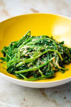 a yellow bowl filled with green vegetables on top of a table