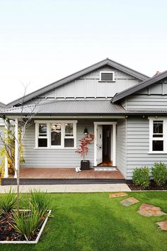 a gray house with white trim and two windows on the front, grass in front