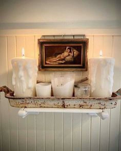 some candles are sitting on a shelf in front of a painting