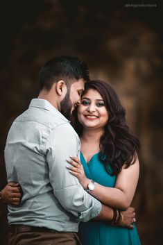 a man and woman embracing each other in front of a dark background with their arms around each other