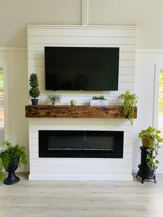 a flat screen tv mounted above a fireplace with potted plants on the mantel