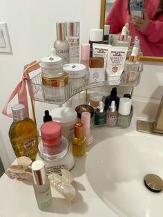 a bathroom sink filled with lots of beauty products on it's shelf next to a woman taking a selfie in the mirror