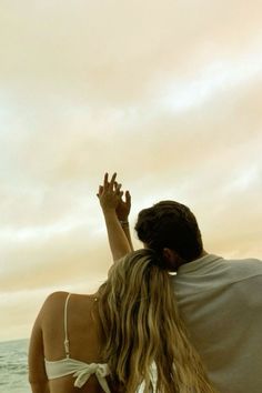 a man and woman are sitting on the beach looking at the water with their arms in the air