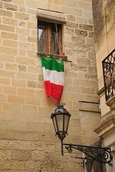 an italian flag hanging from the side of a building next to a lamp post and window