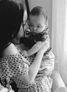 a woman holding a baby in her arms and kissing the child's face with both hands