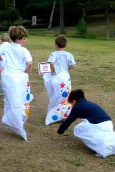 three children in white costumes are playing with kites on the ground and one boy is holding a sign