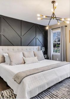 a large white bed sitting under a chandelier in a bedroom next to a window