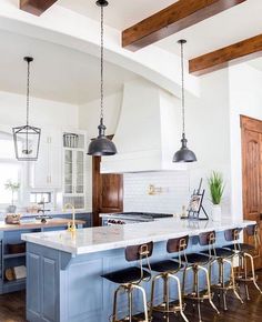 a large kitchen with an island and bar stools in the center, along with several lights hanging from the ceiling