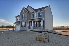 a two story house in the middle of a gravel lot with a rock out front