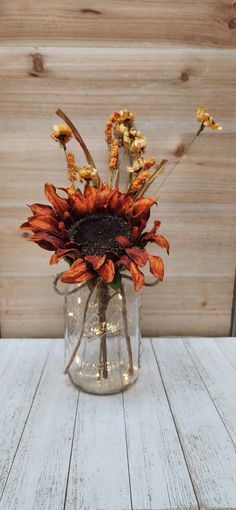 a glass vase filled with flowers on top of a white wooden table next to a wood paneled wall