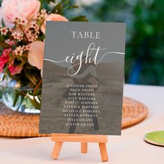 a table sign sitting on top of a wooden easel next to a vase filled with flowers