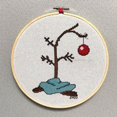 a cross stitched picture of a tree with an ornament hanging from it