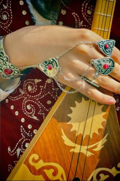 a woman's hand holding onto a guitar string with beads and chains on it