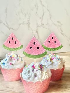 three cupcakes decorated with watermelon slices and sprinkles are sitting on a table