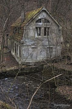 an old abandoned house sitting in the woods next to a stream with no leaves on it