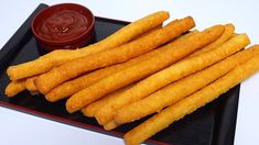 french fries on a black plate with ketchup and dipping sauce in the background