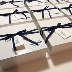 many white boxes with blue ribbons tied around the edges and tags attached to them are stacked on top of each other