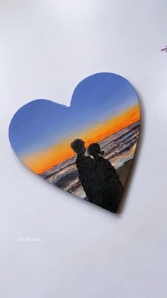 a heart shaped cutout with the silhouette of two people standing in front of an ocean sunset