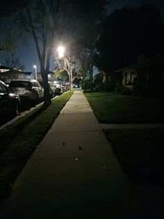 the sidewalk is lined with parked cars and street lights in the distance at night time