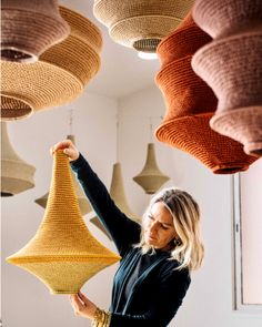 a woman standing in front of some hanging lights with her hands on the light fixture