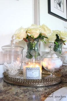 candles and flowers in glass jars on a tray with a mirror behind the candle holder