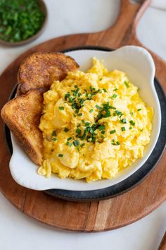 scrambled eggs and toast on a plate with parsley in the bowl next to it