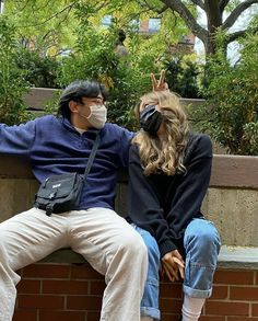 a man and woman sitting on a brick wall wearing face masks while covering their eyes