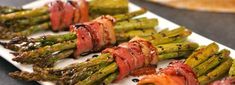 asparagus wrapped in bacon sitting on a white plate next to other food items