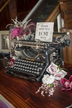 an old fashioned typewriter sitting on top of a wooden table next to pink flowers