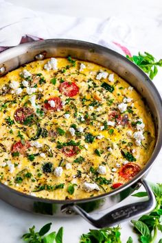 an omelet with tomatoes, cheese and herbs in a pan on a table