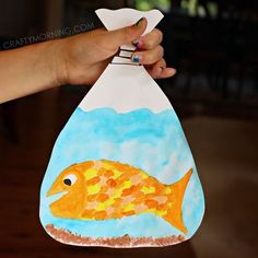 a hand holding up a paper bag with a fish on it and water in the bottom