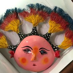 a pink mask with yellow and red hair on it's head is sitting in a white box