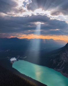 the sun shines through clouds over a mountain lake and mountains in the distance with water below