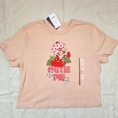 Strawberry Shortcake Graphic Cropped / Baby Tee With "Cutie Pie" And Classic Strawberry Shortcake Design Licensed Shirt By Mad Engine, Sold At Target, Now Sold Out! Nwt, Never Worn Or Washed. Size Small Measured Flat: Pit To Pit 18.5" Waist 17" Hem 18" Back Length 17.5" Color Is A Warm Light Pink With A Slight Peach Tone. It's More Vibrant Than What My Camera Will Pick Up; Photo Of Shirt On Model Shows The Color Most Accurately. Comes From Smoke-Free Home With Cat. Has Been Stored Away From Cat, Trendy Summer Tops From Target, Fitted Pink Top With Strawberry Print, Trendy Pink Top With Strawberry Print, Casual Cotton Tops From Target, Pink Strawberry Print Crew Neck Top, Pink Short Sleeve Sweet Top, Sweet Pink Short Sleeve Top, Cropped Graphic Tees, Vintage Americana