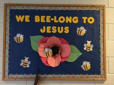 a bulletin board that says we belong to jesus with paper flowers and bees on it