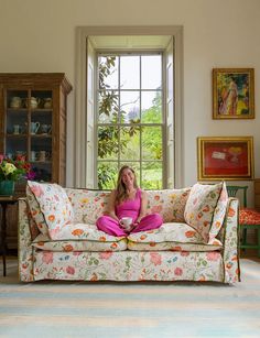 a woman sitting on top of a couch in a living room next to a window