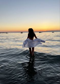 a woman standing in the water at sunset