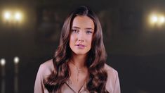 a woman with long brown hair standing in front of two candles and looking at the camera