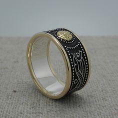 a gold and black wedding ring with an intricate design on the inside, sitting on a beige surface