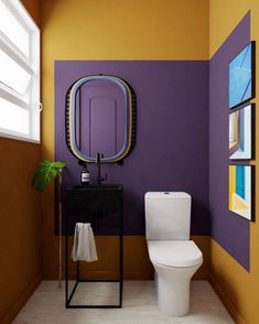 a white toilet sitting in a bathroom next to a purple and yellow wall with pictures on it