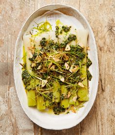 a white bowl filled with green vegetables on top of a wooden table next to a knife and fork