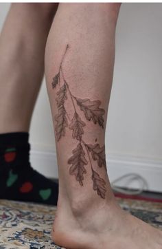 a woman's leg with leaves on it and a tattoo design on the side