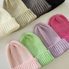 six colors of knit beanie hats laid out on a white surface, with one in the middle