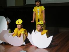 three children in yellow costumes are sitting on the floor with paper cut out to look like eggs