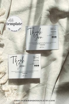 two business cards sitting on top of a white sheet covered in paper with the words thank you