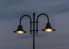 two street lamps on top of a pole with cloudy sky in the background at night