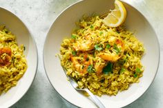 two white bowls filled with rice and shrimp next to a lemon wedge on the side