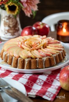 an apple cake on a white plate with apples in the background and a red checkered table cloth